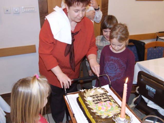 Mami Vanja pri razrezu torte; dogodek spremljajo Maruša, Manca in Tonči
